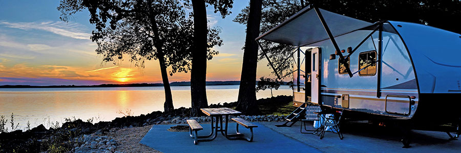 camper and picnic table beside a a lake at sunset