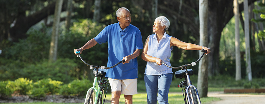 Senior couple walking with bicycles on a park path, smiling together.