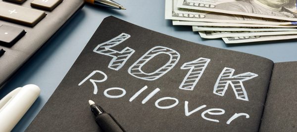 Notebook labeled ‘401(k) Rollover’ on a desk with a calculator, pen, and cash, representing retirement planning.